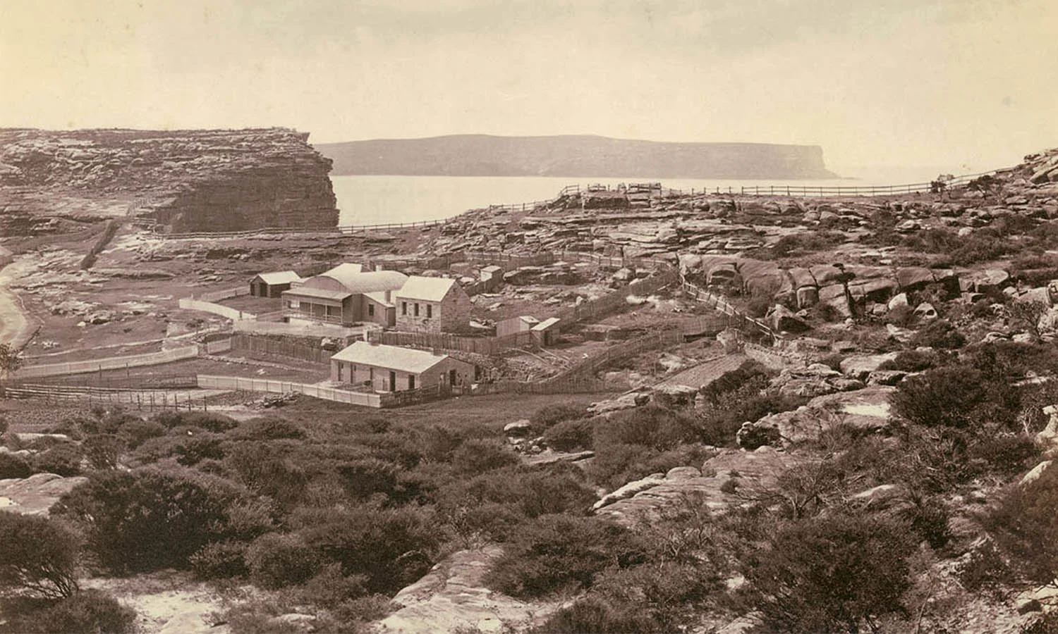 Barren ground with several small buildings and a few trees in the background.