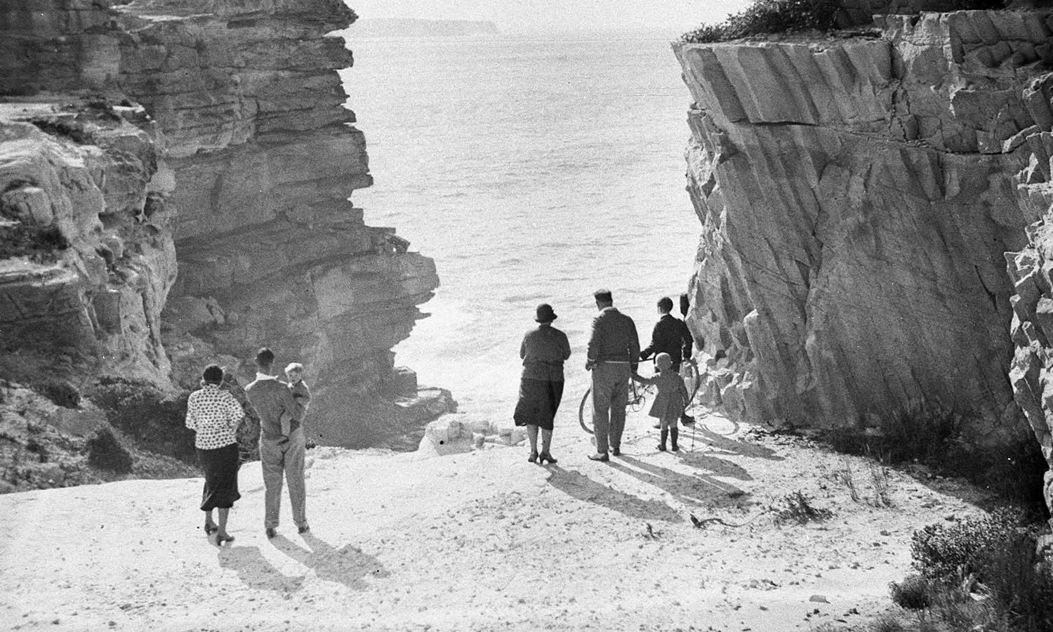 People looking over cliff edge at ocean below.